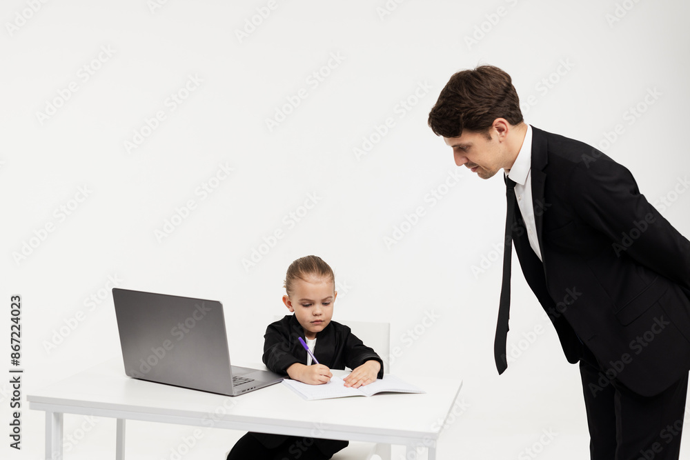 A business little girl in a stylish formal suit signs documents at her desk against a light background. Concept of business, finance and children's emotions. A business little girl in a stylish formal suit signs documents at her desk against a light background. Concept of business, finance and children's emotions.
