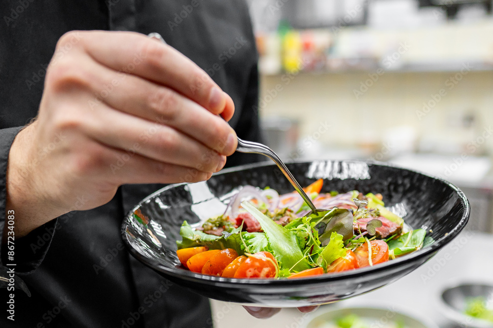 A person in a black outfit garnishes a fresh salad with tongs A person in a black outfit garnishes a fresh salad with tongs