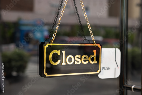 A sign hanging from a window that says "closed" in gold letters