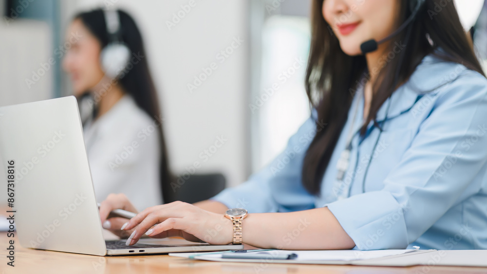 Smiling call center agents wearing headsets, working at desks with computers and documents in a modern office. Soft focus Smiling call center agents wearing headsets, working at desks with computers and documents in a modern office. Soft focus
