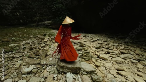 An Asian girl in a beautiful red kimono and a Vietnamese triangular hat is dancing sexually in nature in a rocky canyon