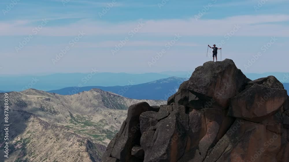 A young man raises his arms victoriously at the top of the mountain A young man raises his arms victoriously at the top of the mountain