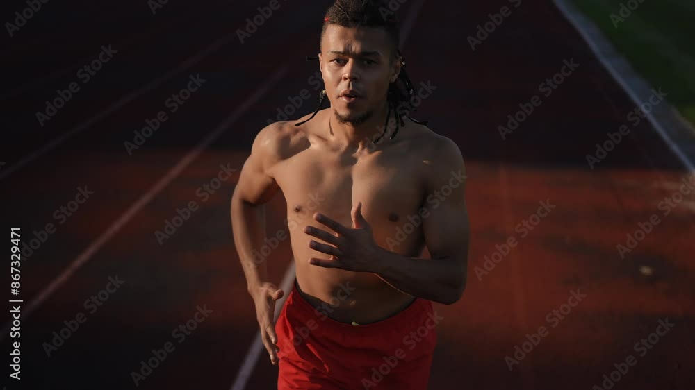 Slow motion. Medium shot. A high-angle shot. An athlete in scarlet men's athletic shorts, breathing heavily, is running on the running track of the city stadium on an autumn day Slow motion. Medium shot. A high-angle shot. An athlete in scarlet men's athletic shorts, breathing heavily, is running on the running track of the city stadium on an autumn day