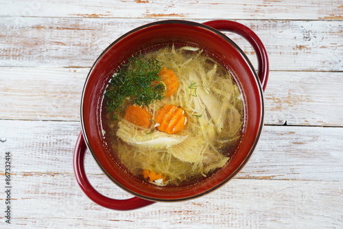 Chicken soup, chicken broth, with pieces of chicken and vegetables in red bowl with handles . Chicken bouillon, boiled meat