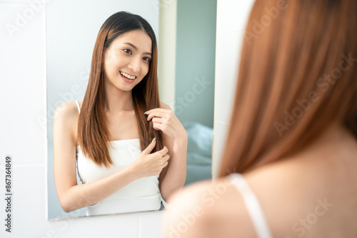 Self confident women look in the mirror brush up their hair and admire their body. Young asian beautiful woman who takes care of herself well. Check facial skin