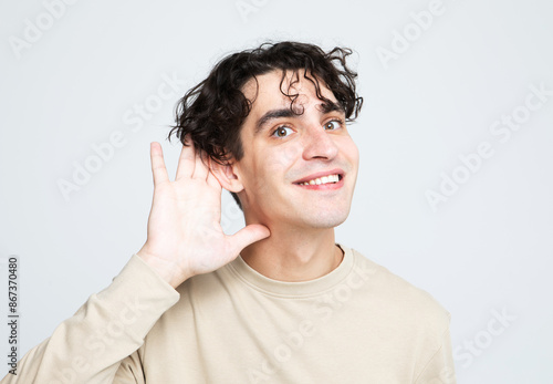 Young handsome man hearing something and smiling over light grey background. © Raisa Kanareva