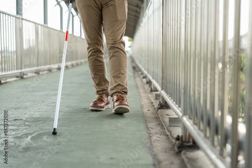 Young blind man walking in city with walking stick. Visually impaired man difficult to traveling on the road wearing sun glasses Cross the road cross the footbridge photo