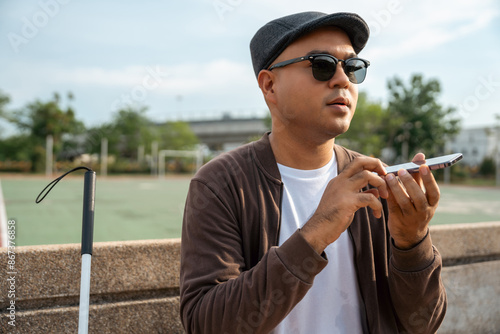 Young asian blind man using application on mobile phone to helping accessibility for persons with visual impairment. Technology for blind people sending voice message or navigation. photo