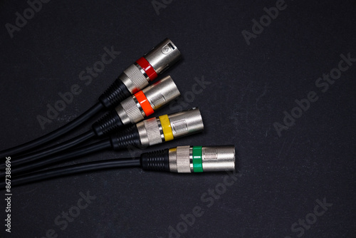 XLR audio cables on black background with metallic coloured connectors with different coloured indicators.