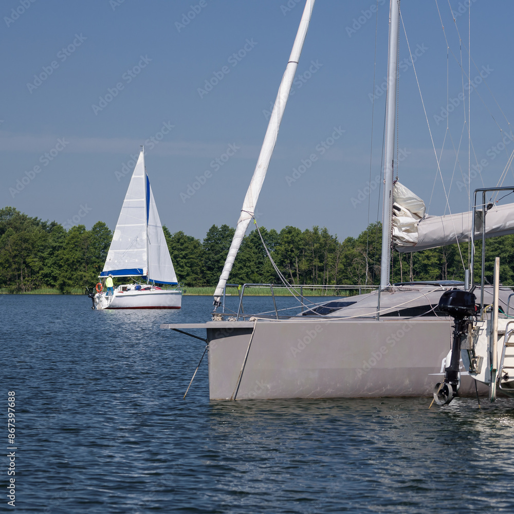 LANDSCAPE BY THE LAKE - A sailboat sails on the lake and yachts in marina in the foreground
LANDSCAPE BY THE LAKE - A sailboat sails on the lake and yachts in marina in the foreground