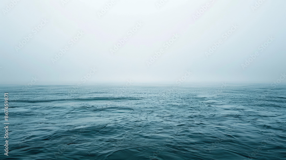 Obraz premium A vast expanse of ocean under a foggy sky can be seen. The water is calm but exhibits slight ripples, and the horizon is barely visible through the mist.