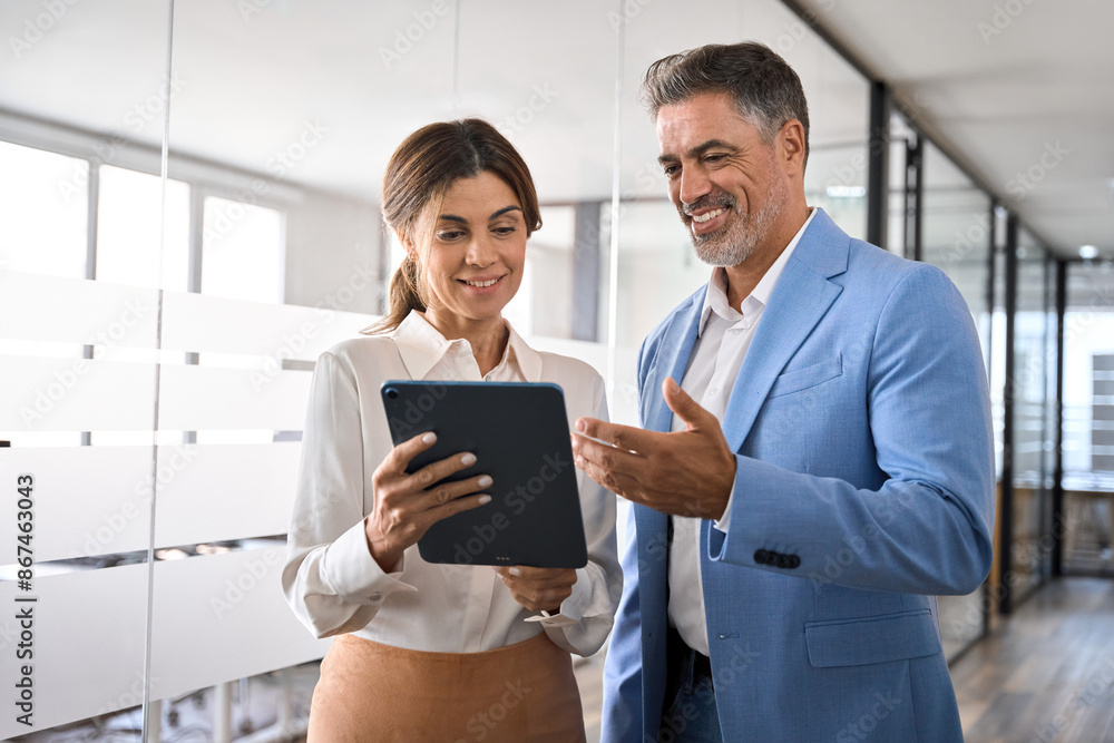 © insta_photos - Professional mature business people, two happy middle aged business man and woman executives partners team working together checking corporate results collaborating standing in company office. © insta_photos - Professional mature business people, two happy middle aged business man and woman executives partners team working together checking corporate results collaborating standing in company office.