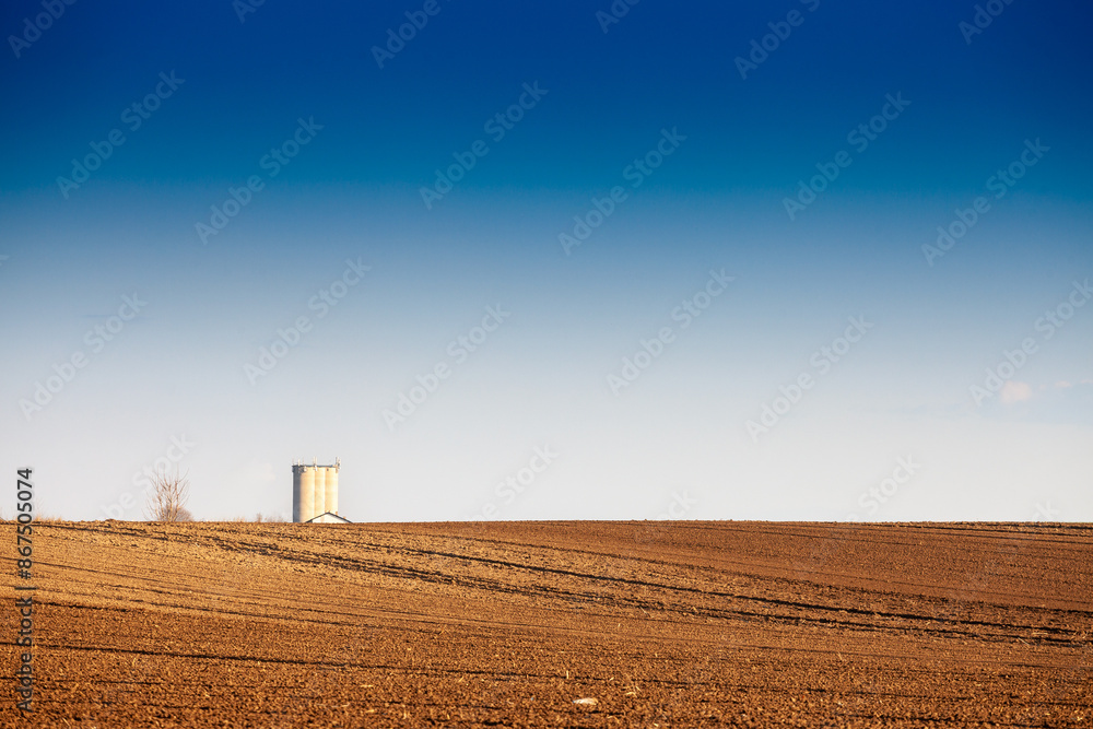 Φωτογραφία Picture of a plowed field with furrows on a sunny afternoon with blue sky in serbia, in deliblatska pescara with a silo in background