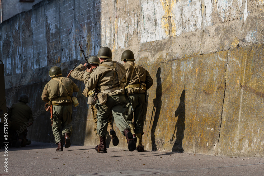 World War II infantry division soldiers run along a wall during a combat in the city. View from behind World War II infantry division soldiers run along a wall during a combat in the city. View from behind