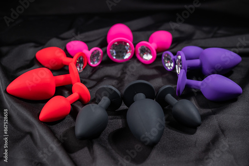 A set of silicone anal plugs in different colors and sizes on a black silk sheet. 