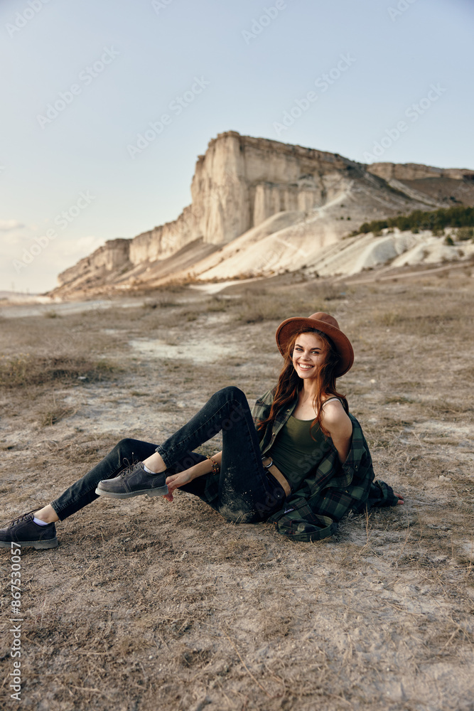 Serene woman sitting in front of majestic mountain wearing stylish hat Serene woman sitting in front of majestic mountain wearing stylish hat