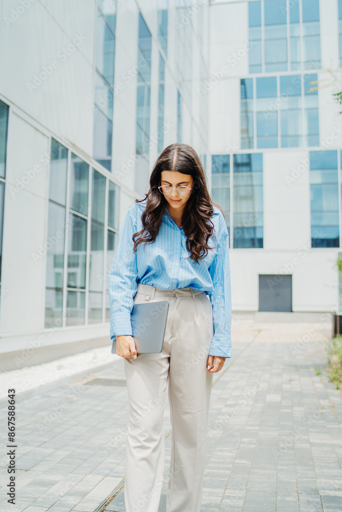 One beautiful young successful business woman going to work at business office modern building while holding laptop and waring glasses One beautiful young successful business woman going to work at business office modern building while holding laptop and waring glasses