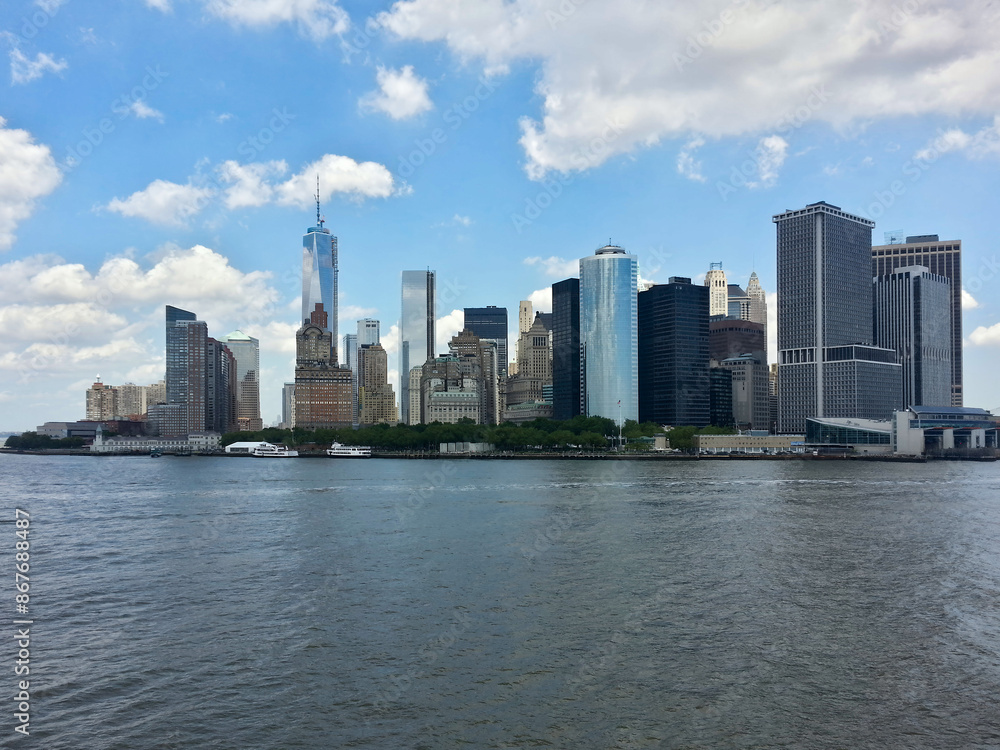 New York City's Manhattan skyline, captured from across the Hudson River. The iconic One World Trade Center stands tall among skyscrapers, with ferry boats visible along the waterfront on a sunny day. New York City's Manhattan skyline, captured from across the Hudson River. The iconic One World Trade Center stands tall among skyscrapers, with ferry boats visible along the waterfront on a sunny day.