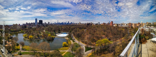 Breathtaking aerial perspective of Central Park's lush greenery and serene lake, juxtaposed against the iconic Manhattan skyline on a bright spring day.