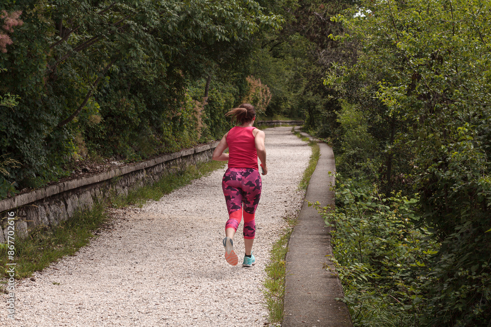 Obraz premium A young female athlete from behind is running on a countryside path