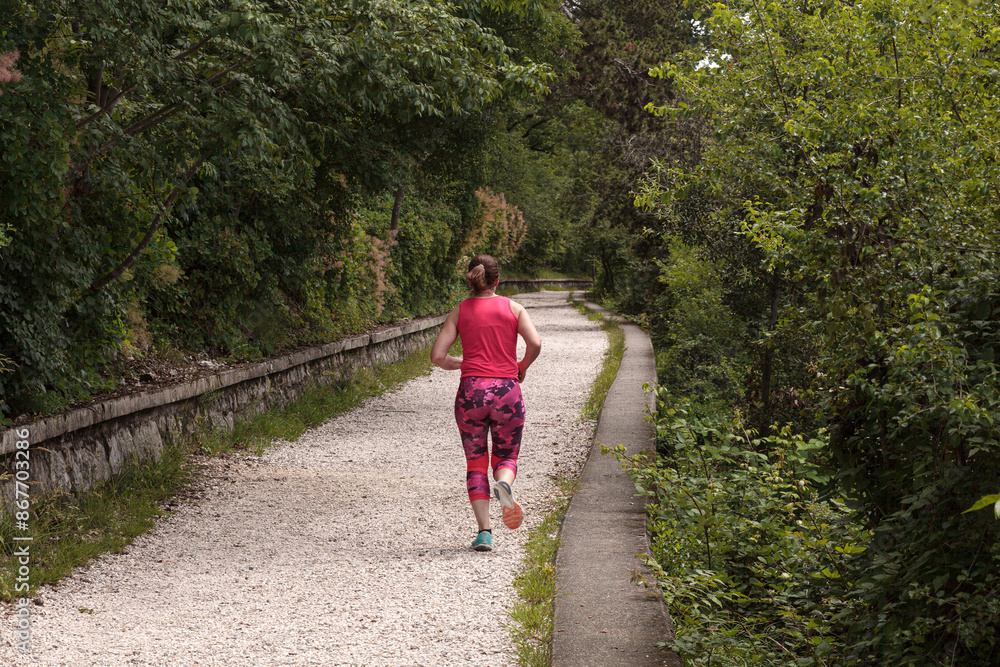 Obraz premium A young female athlete from behind is running on a countryside path