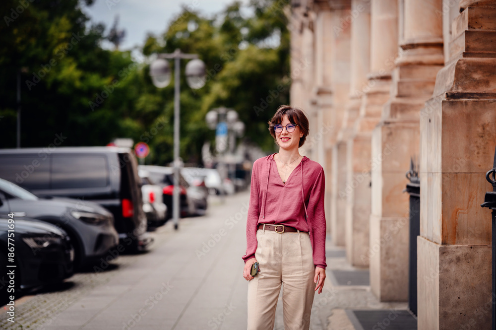 Woman in casual attire smiling while walking on a city sidewalk lined with parked cars and buildings. Woman in casual attire smiling while walking on a city sidewalk lined with parked cars and buildings.
