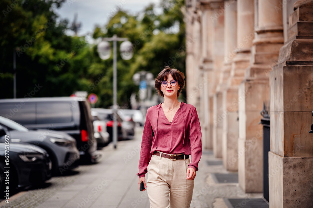 Woman in casual attire smiling while walking on a city sidewalk lined with parked cars and buildings. Woman in casual attire smiling while walking on a city sidewalk lined with parked cars and buildings.
