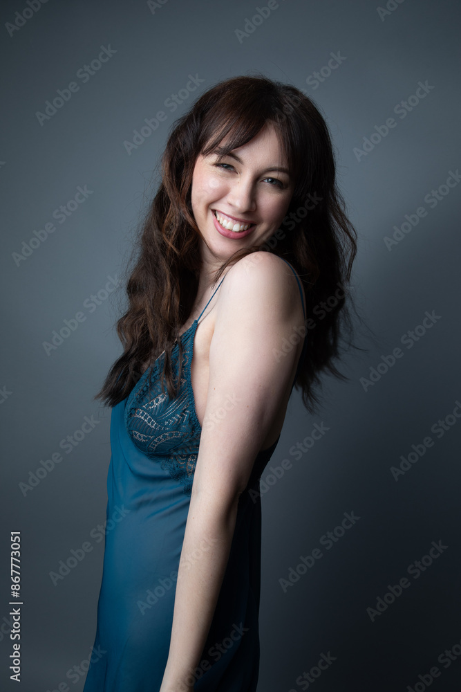 Studio portrait of a beautiful caucasian woman in her 30s wearing a dark blue night gown. She is smiling and looking at the camera. The studio background is grey. Studio portrait of a beautiful caucasian woman in her 30s wearing a dark blue night gown. She is smiling and looking at the camera. The studio background is grey.