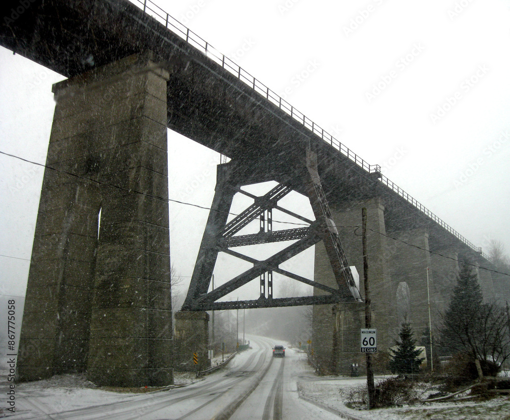 Fototapeta premium Driving under an old railway trestle bridge during a snowstorm.