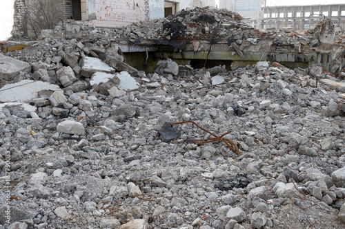 Grey concrete debris with protruding fittings against the remains of destroyed buildings. Background
