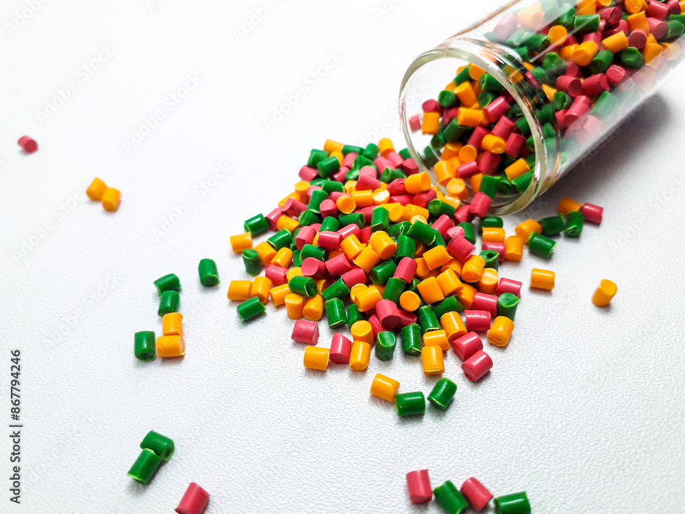 Colorful mixed masterbatch granules spilling from a glass tube on a white background.Color pigment carrier polymers in the plastics industry Colorful mixed masterbatch granules spilling from a glass tube on a white background.Color pigment carrier polymers in the plastics industry