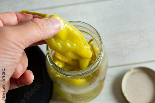 A view of a hand pulling out a pickled pepperoncini pepper from a jar. photo