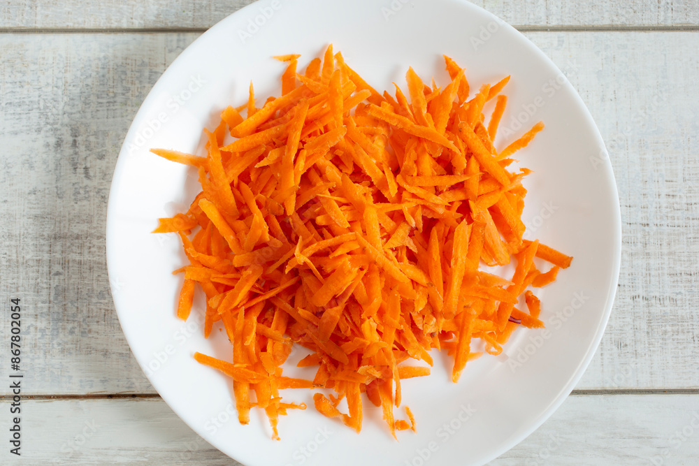 A top down view of a plate of shredded orange carrots. A top down view of a plate of shredded orange carrots.