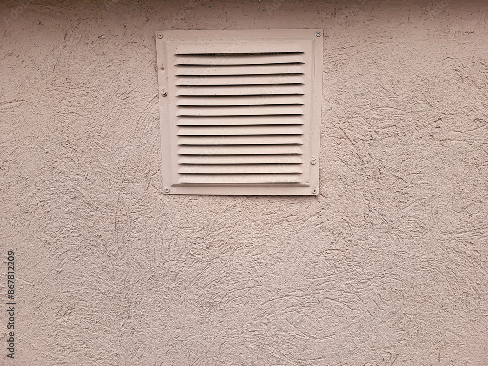 A square ventilation grille with a pattern of metal stripes on a pink plastered wall A square ventilation grille with a pattern of metal stripes on a pink plastered wall