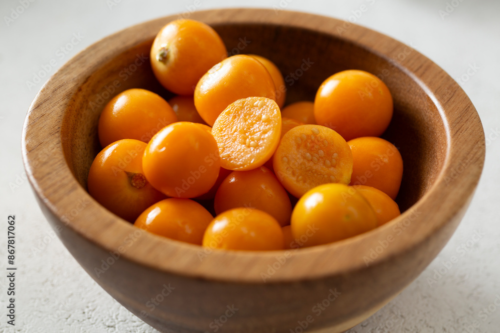 A view of a small wooden bowl of orange gooseberries. A view of a small wooden bowl of orange gooseberries.