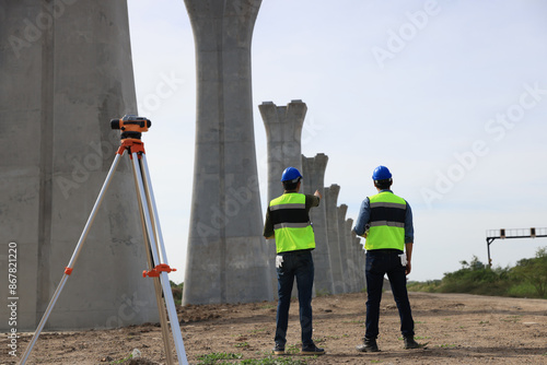 Survey construction technicians wearing safety vests and hard hats work with level survey cameras at road construction site