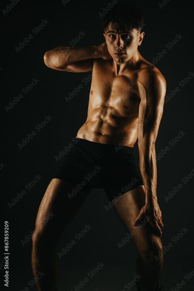 Naklejka premium Fit man displaying his toned abs in a dramatic light setting, focusing on his athletic body and fitness.
