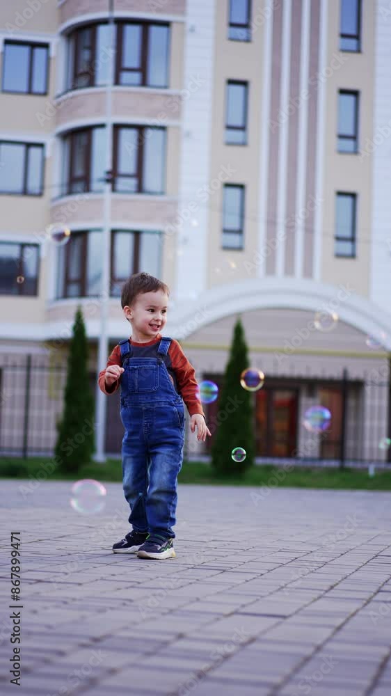 Energetic happy Caucasian toddler runs to catch soap bubbles. Cheerful three-year-old baby having active time outdoors. Vertical video. Energetic happy Caucasian toddler runs to catch soap bubbles. Cheerful three-year-old baby having active time outdoors. Vertical video.