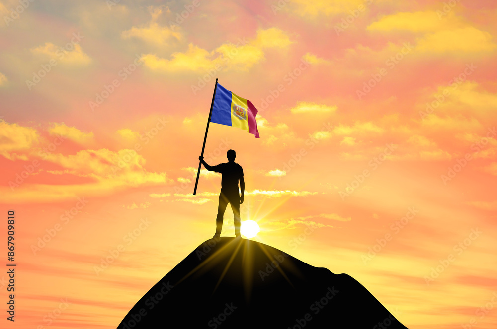 Waving flag of Andorra at the top of a mountain summit against sunset or sunrise. Andorra flag for Independence Day. Waving flag of Andorra at the top of a mountain summit against sunset or sunrise. Andorra flag for Independence Day.