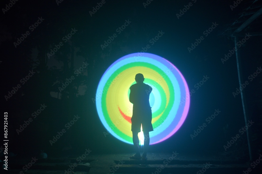 One person standing alone against a Colourful circle light painting as the backdrop
One person standing alone against a Colourful circle light painting as the backdrop
