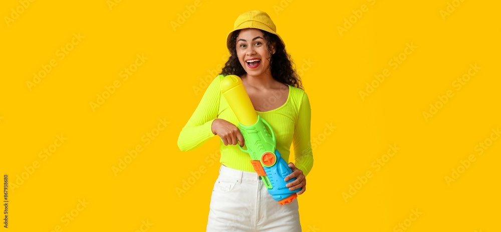 Happy African-American woman with water gun on yellow background