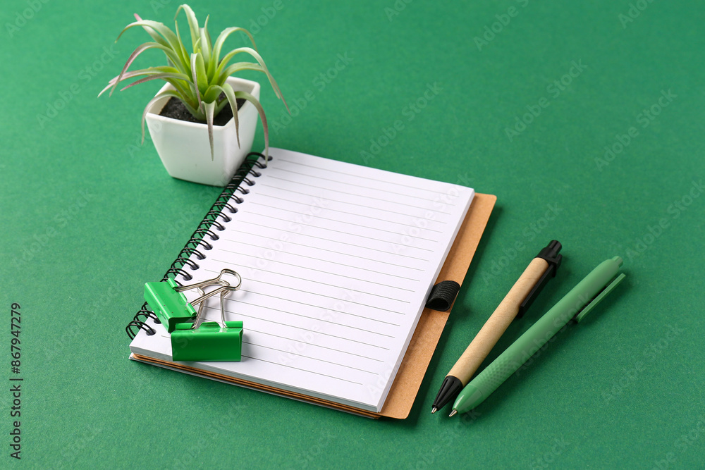 Notebook with pens and plant on green background Notebook with pens and plant on green background