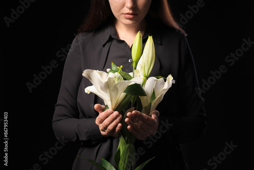 Young woman with funeral bouquet of lily flowers on black background, closeup