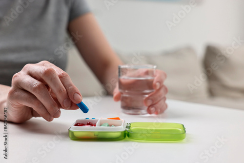 Woman with pills, organizer and glass of water at white table, closeup