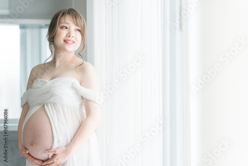 Free Download 家のカーテンの前でマタニティフォトの撮影をする妊婦のアジア人女性
 - GFXLoad