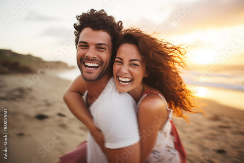 Young couple in their thirties on the beach laughing while riding piggyback at sunset