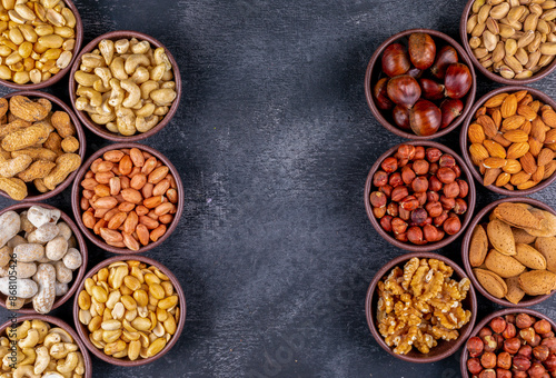 Flat lay assorted nuts and dried fruits in mini different bowls with pecan, pistachios, almond, peanut, on black stone background. horizontal free space for your text