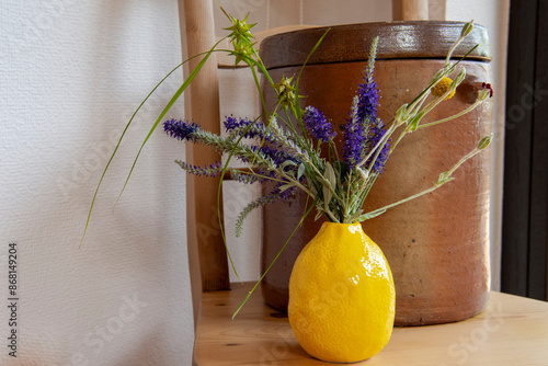 Schöne sommerliche Küchendekoration- Eine gelbe Vase mit Sommerblumen vor einem Tongefäß photo