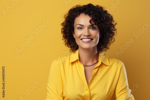 Portrait of smiling woman in yellow shirt looking at camera over yellow background © Stocknterias