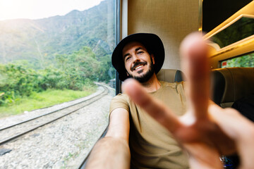 Young happy man traveling by train during summer vacation. Joyful male taking selfie on Peru tourist rail train travel from Ollantaytambo to Machu Picchu. Adventure concept.